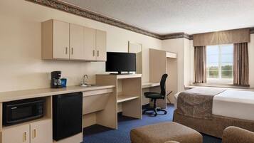 A hotel room with a kitchenette, a bed, a desk, and a television.
