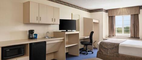 A hotel room with a kitchenette, a bed, a desk, and a television.