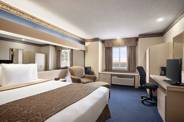 Habitación de hotel con una cama grande, un escritorio con computadora, una silla, un televisor y una ventana con cortinas.