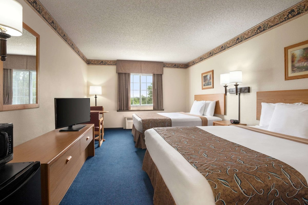 Quarto de hotel com uma cama grande, uma escrivaninha com televisão, uma cadeira e uma janela com cortinas.