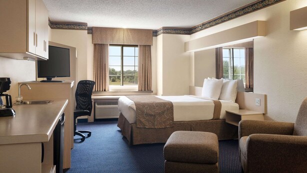 Quarto de hotel com cama, escrivaninha com cafeteira, cadeira e televisão.