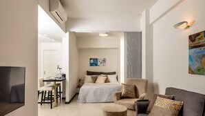 A modern hotel room with a bed, a sofa, a small round ottoman, a desk with a chair, and a TV. - MyFlorenceHoliday Gold Bridge (Florence)