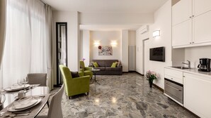 A modern hotel room with a dining area, a living room with a sofa and green armchairs, a kitchen with white cabinets, and a stone floor. - MyFlorenceHoliday Gold Bridge (Florence)