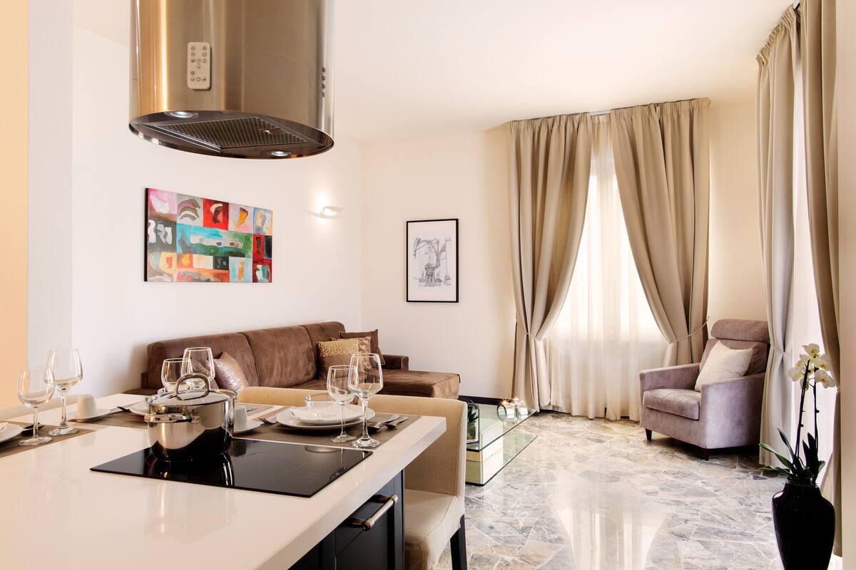 A modern living room with a dining area, a sofa, a chair, and a large window with curtains.