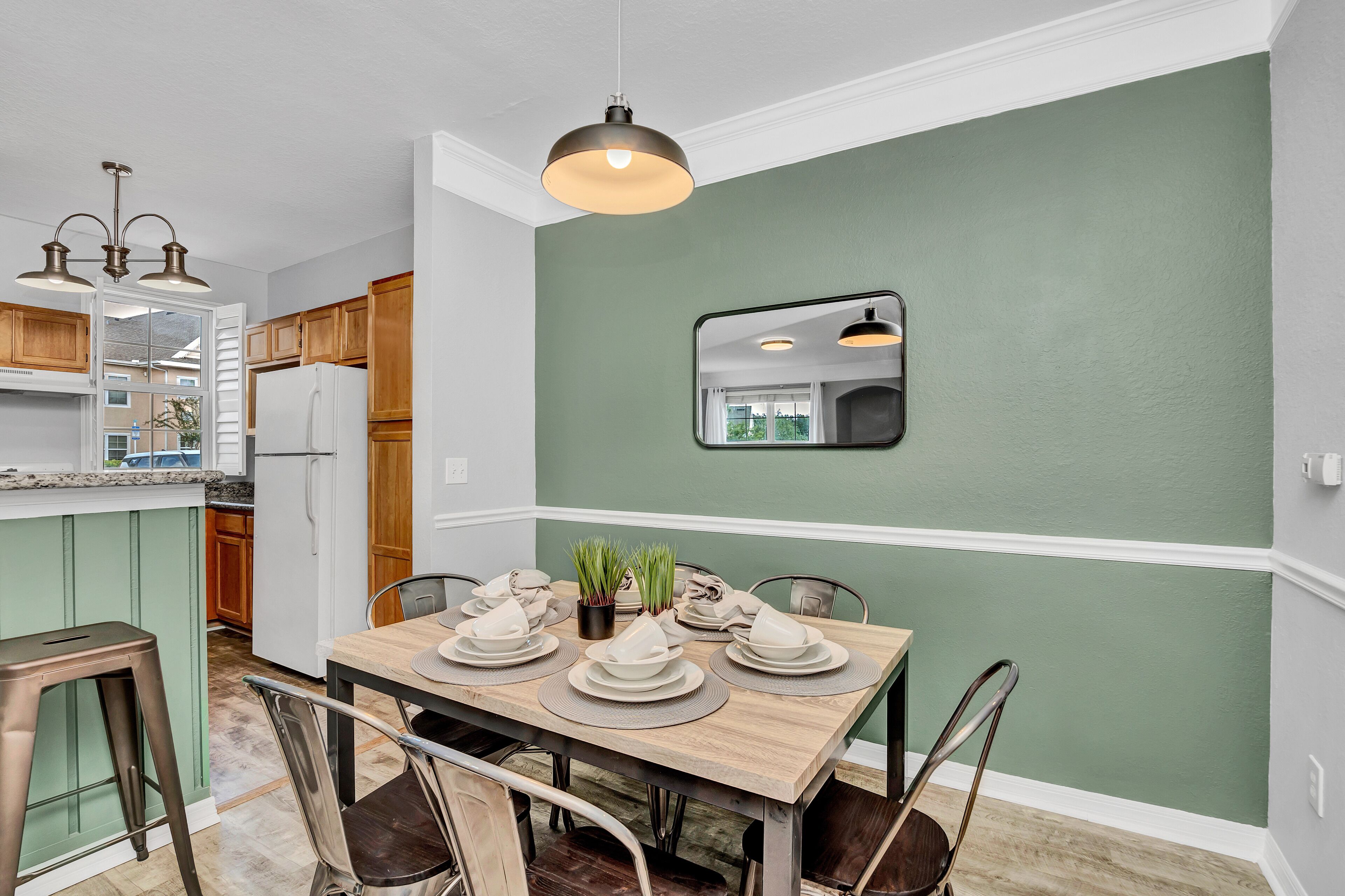 Un comedor con una mesa de madera dispuesta para cuatro personas, una pared de acento verde y una lámpara colgante arriba.