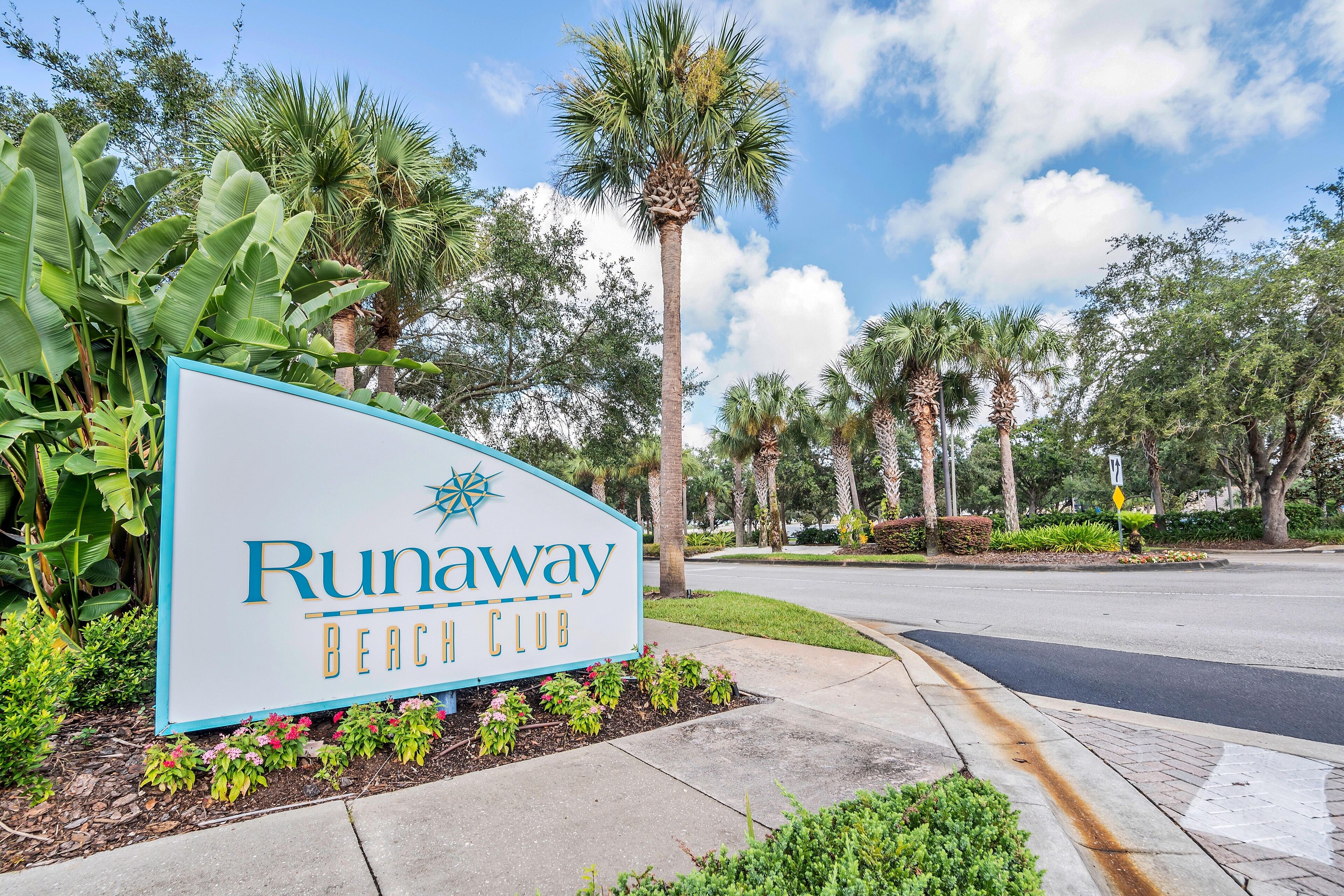 A sign for Runaway Beach Club surrounded by lush greenery and palm trees.