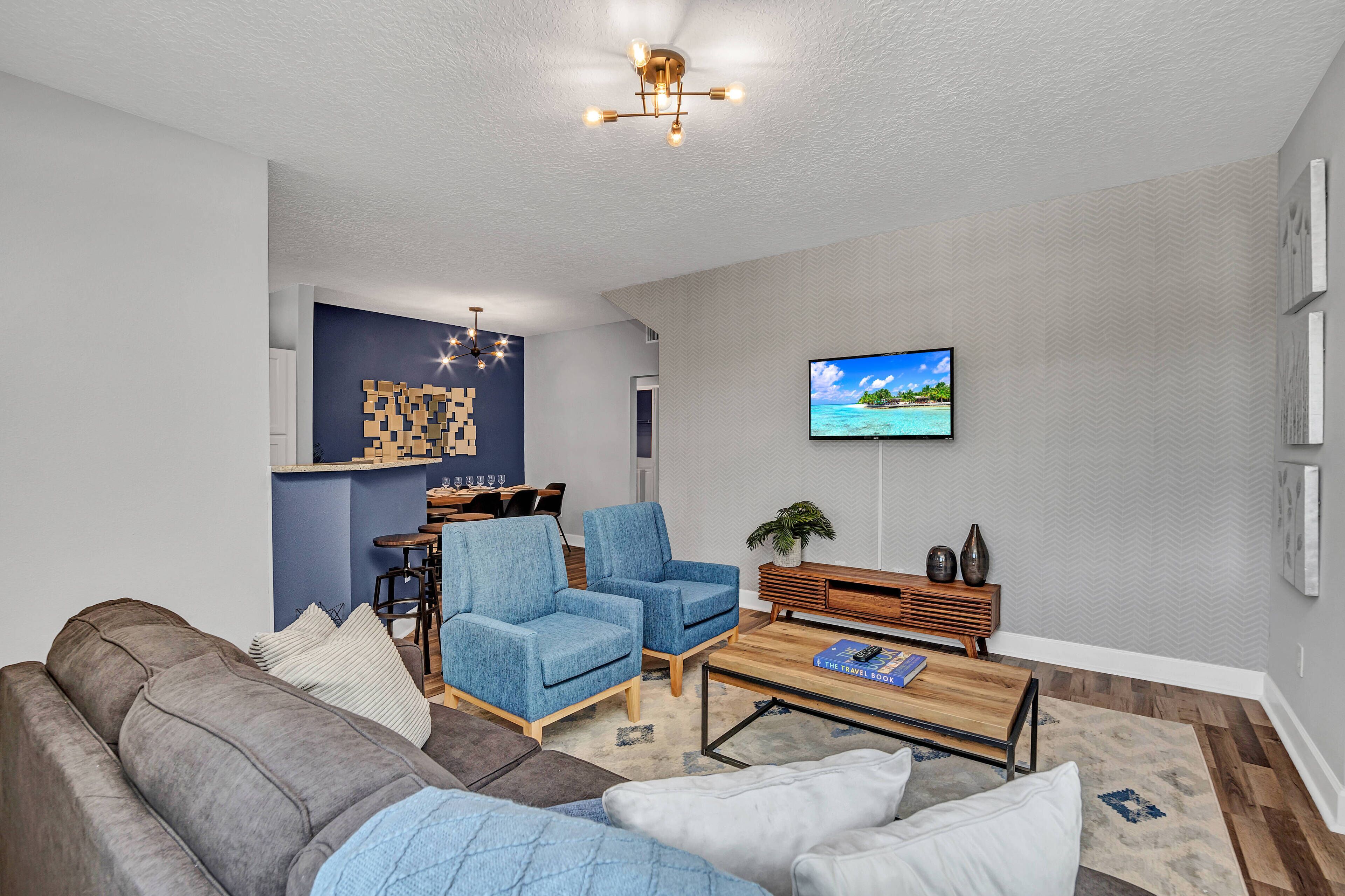 Un soggiorno moderno con un divano grigio, poltrone blu, un tavolino in legno e una TV a parete.