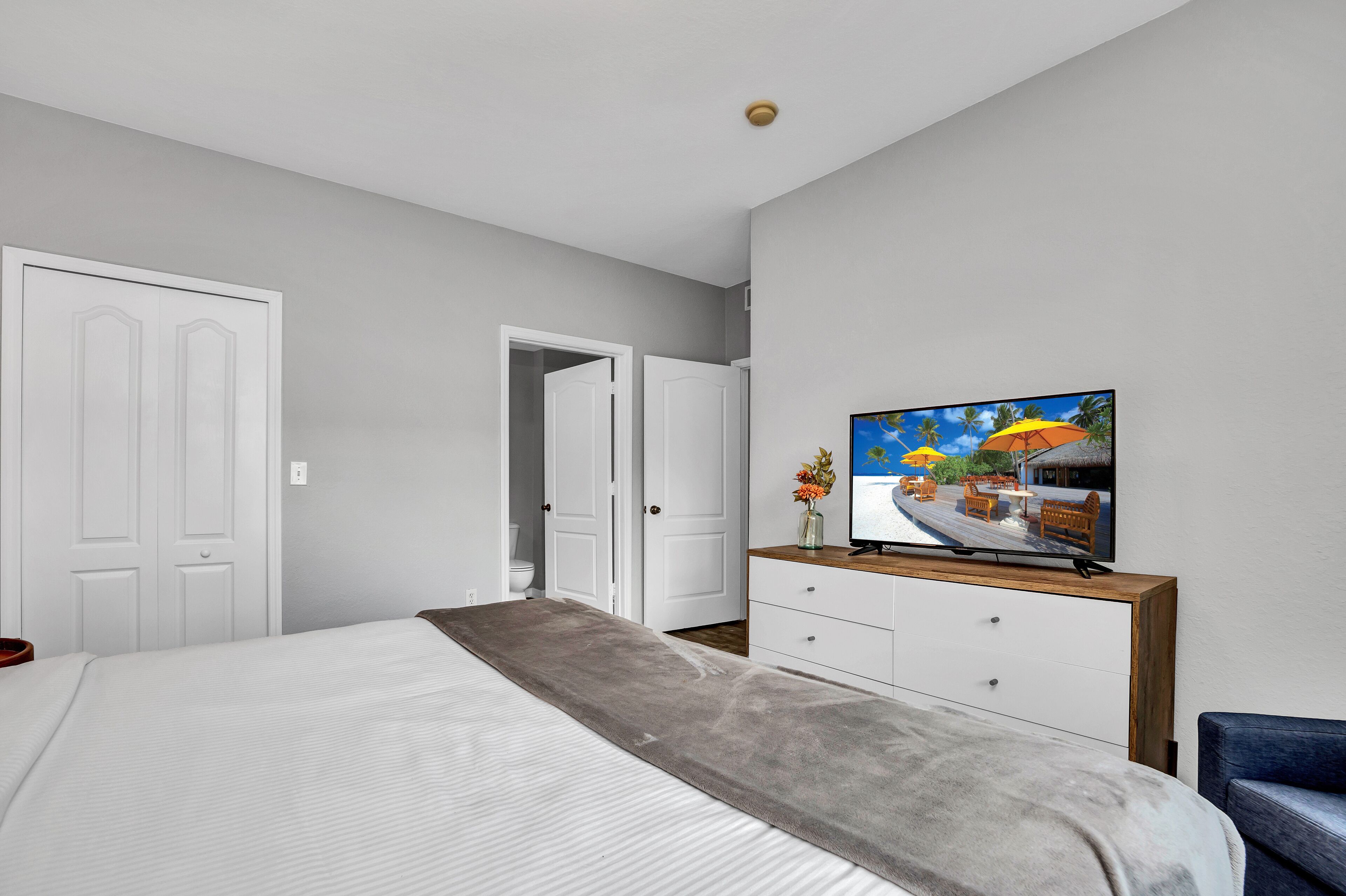 A bedroom with a bed, a TV, a dresser, and a door leading to another room.