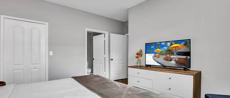 A bedroom with a bed, a TV, a dresser, and a door leading to another room.