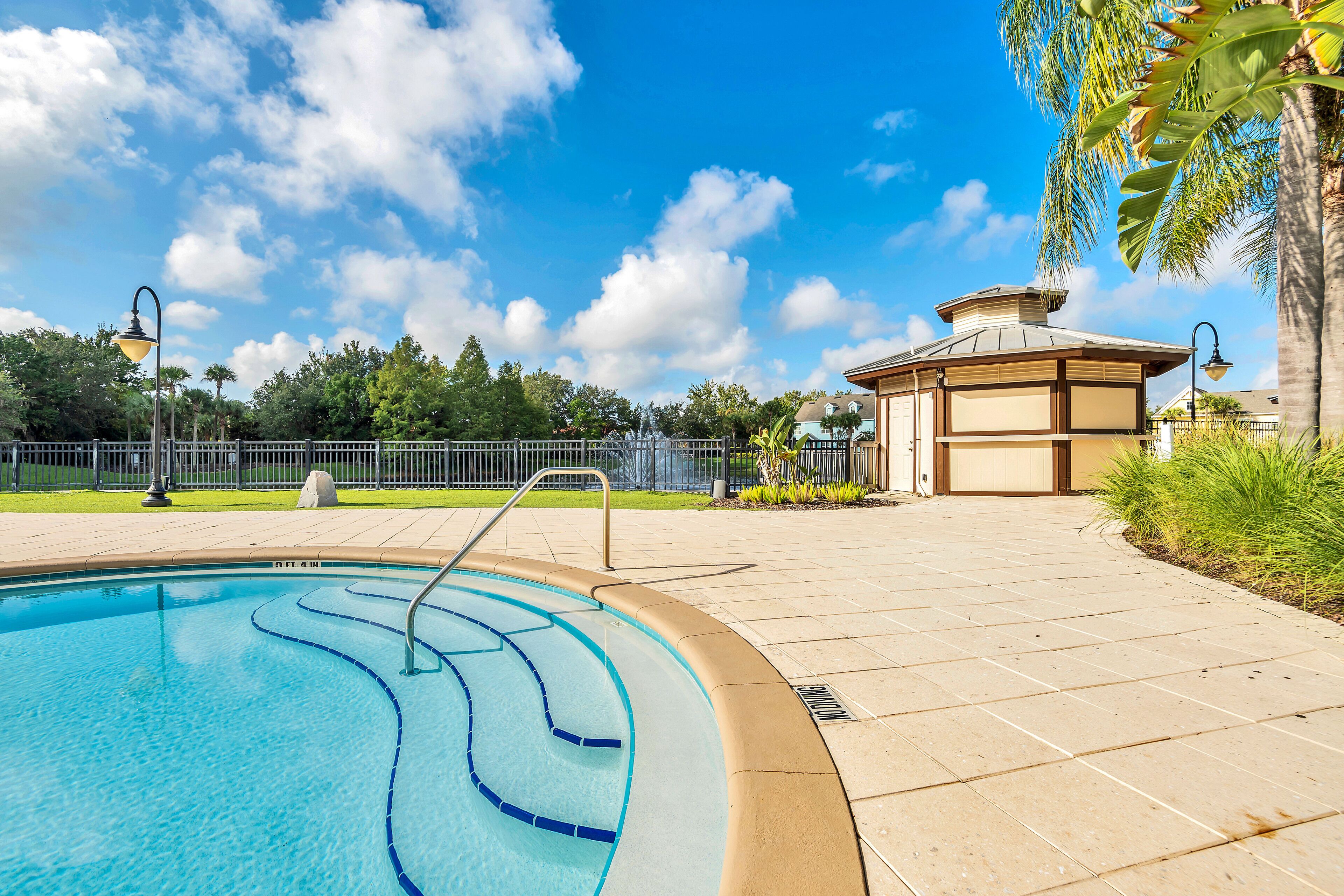 A swimming pool with a tiled deck, a gazebo, and a fence in the background.