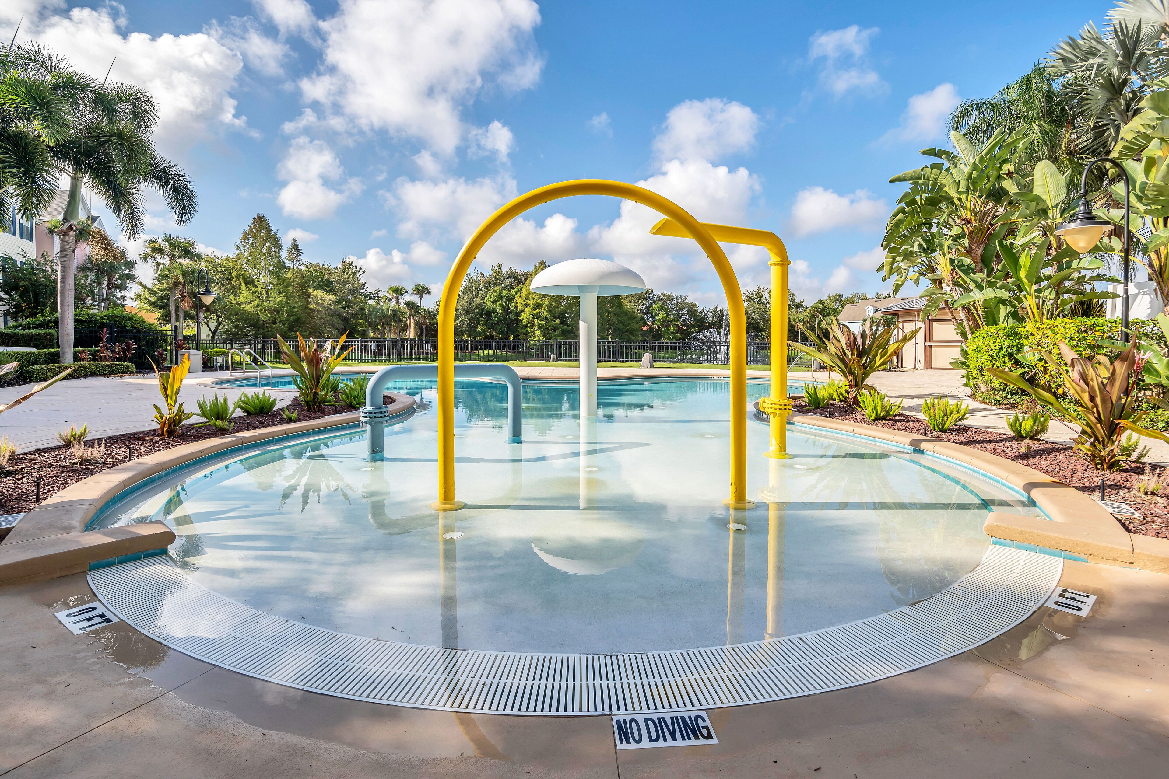 A swimming pool with a 'NO DIVING' sign, surrounded by tropical plants and a clear blue sky.