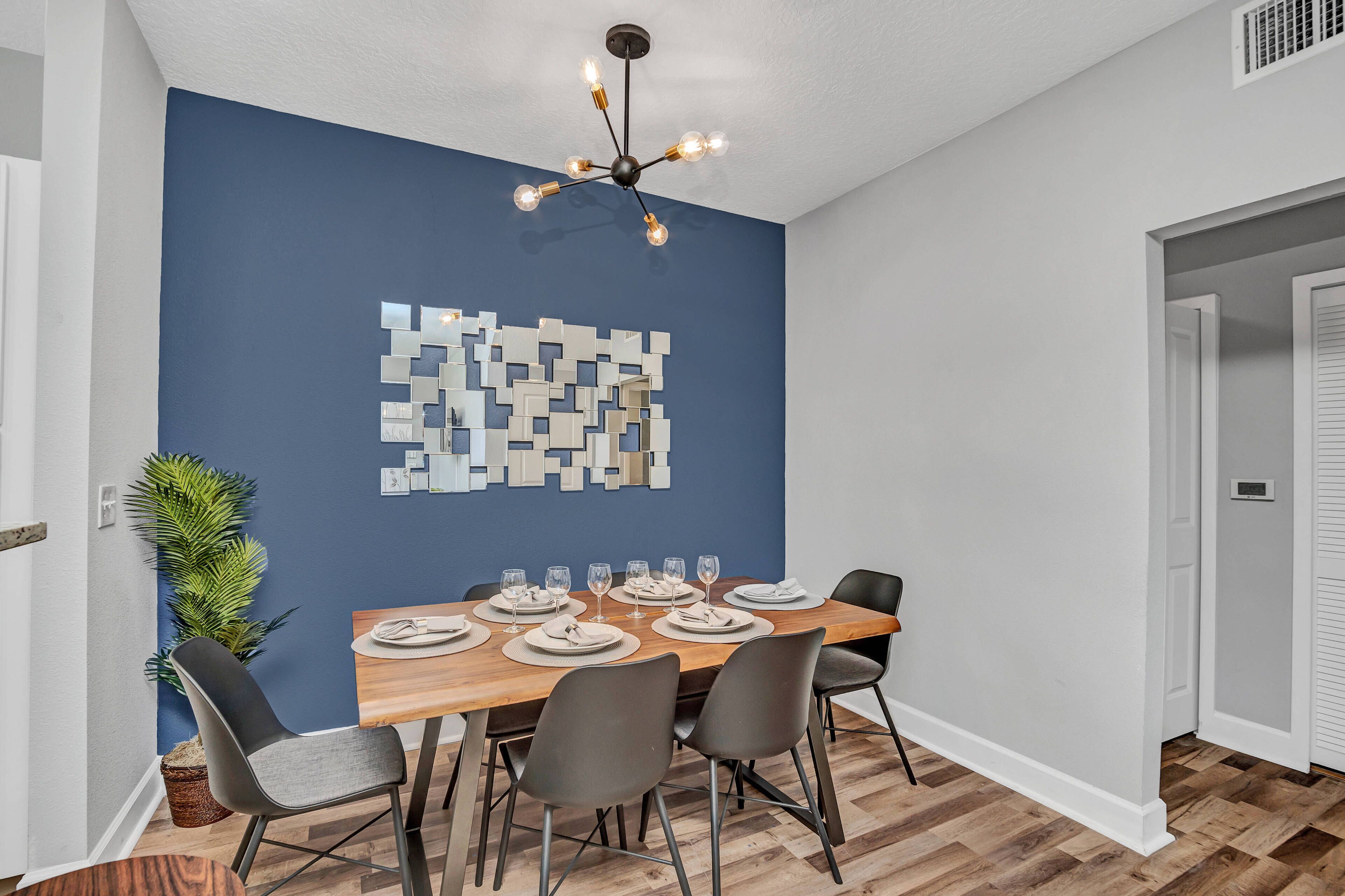 Un coin repas avec une table en bois dressée pour six personnes, six chaises et un luminaire moderne au plafond.