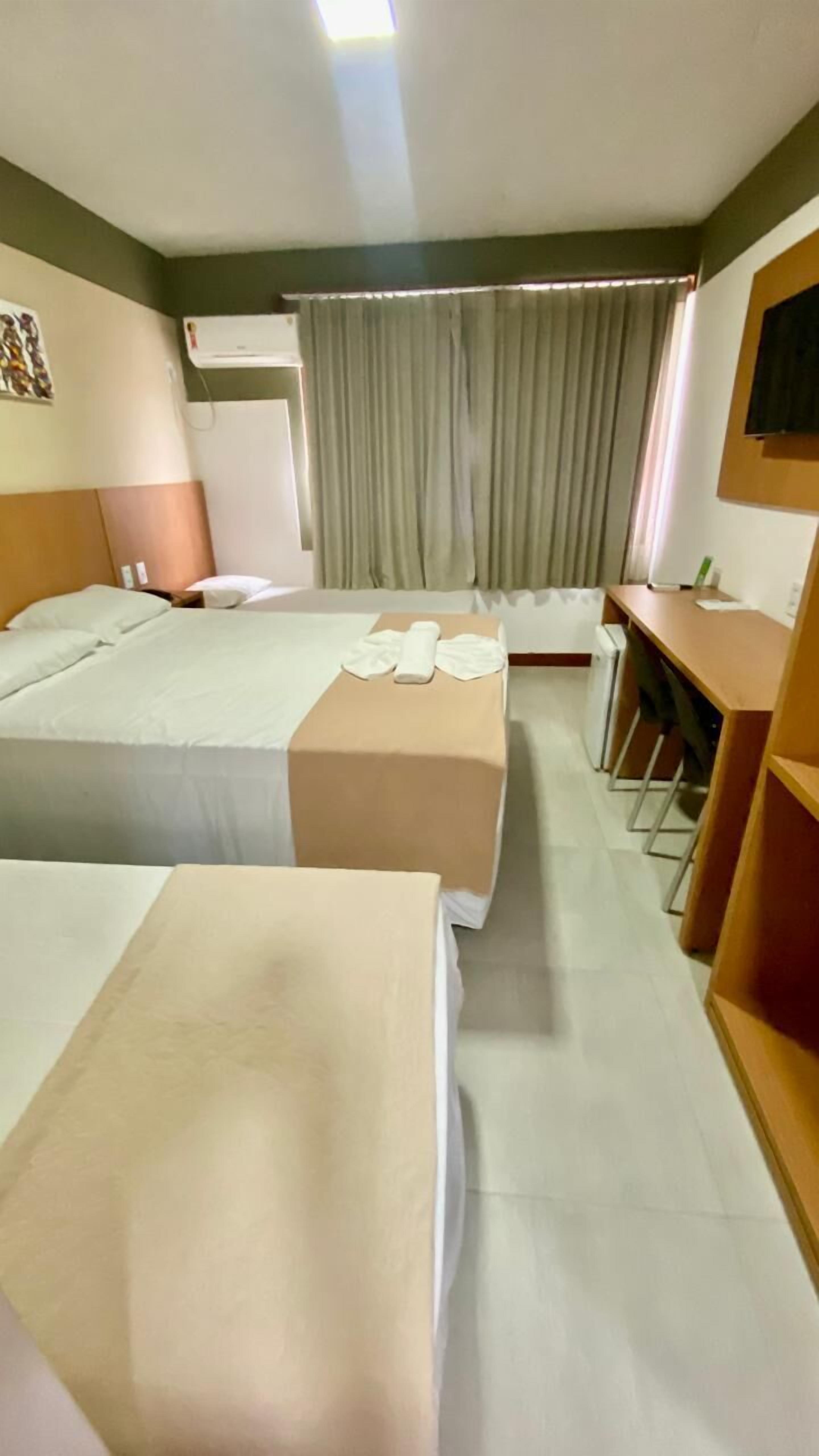 A hotel room with two beds, a desk, a chair, an air conditioner, and a window with curtains.