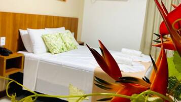 Quarto de hotel com cama, mesa de cabeceira, aparelho de ar condicionado e um quadro colorido na parede.