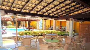An outdoor patio area with wicker furniture and a pool in the background. - Marinas Pousada (Ilhéus)