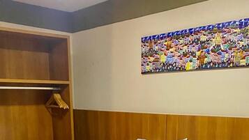 A hotel room with a neatly made bed, a wooden wardrobe, a nightstand with a phone, and a colorful wall mural.