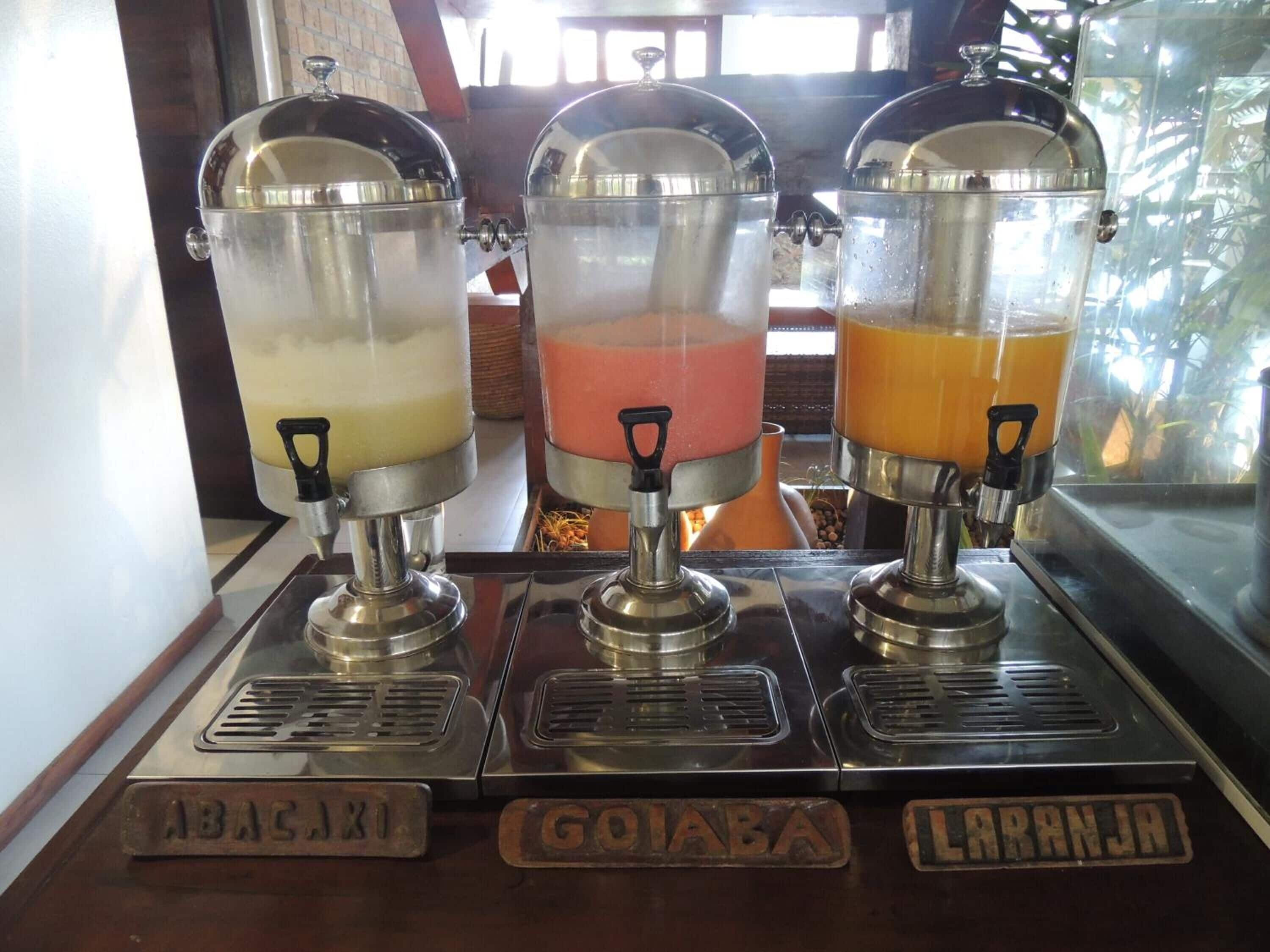Three beverage dispensers labeled 'ABACAXI', 'GOIABA', and 'LARANJA' with different colored drinks.