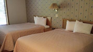 A hotel room with two beds, a window with blinds, a patterned wall, and a wall-mounted lamp.