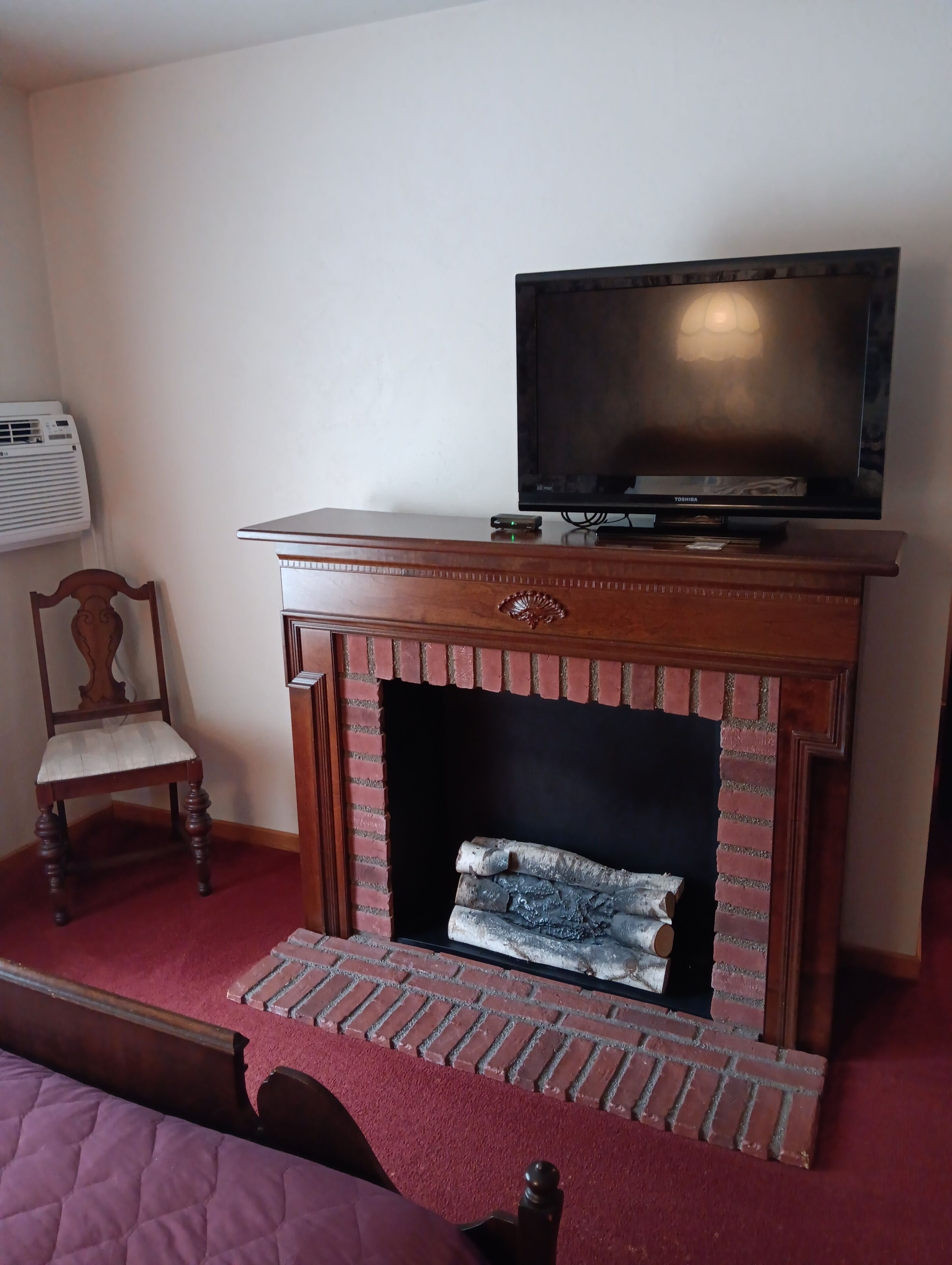 A room with a fireplace, a television on a wooden stand, a chair, and a red carpet.