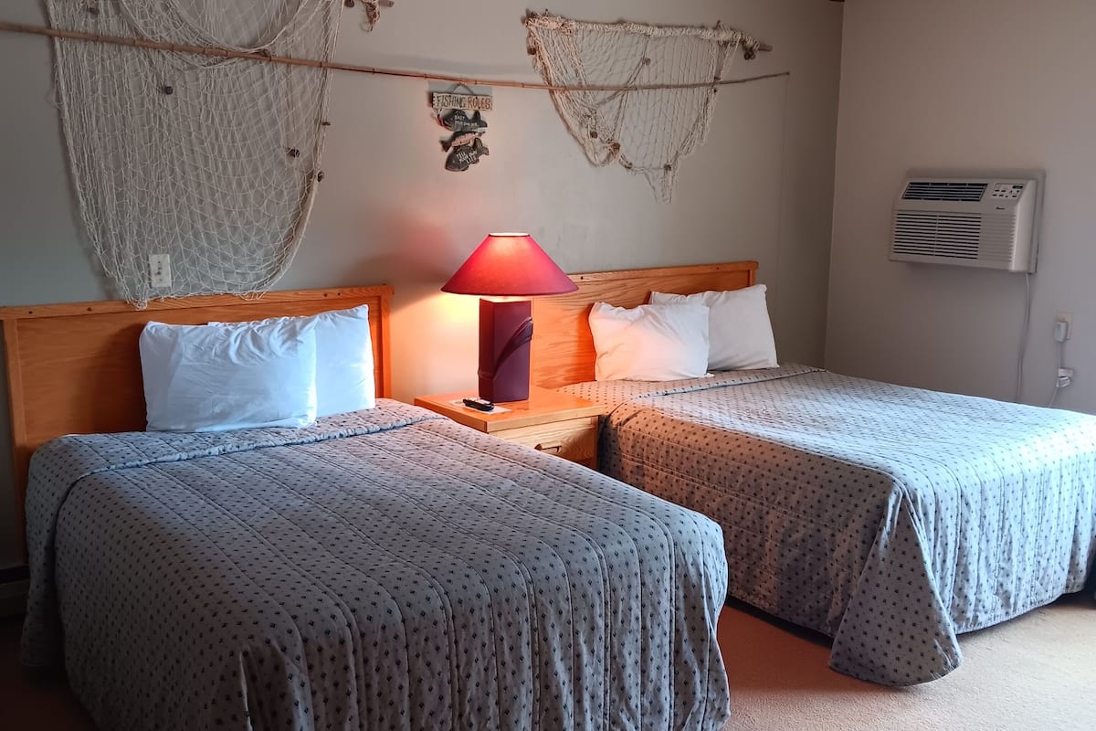 A hotel room with two beds, a wooden headboard, a red lamp, and decorative fishing nets on the wall.