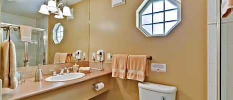 A bathroom with a beige wall, a round mirror, a sink, a toilet, and a shower area.