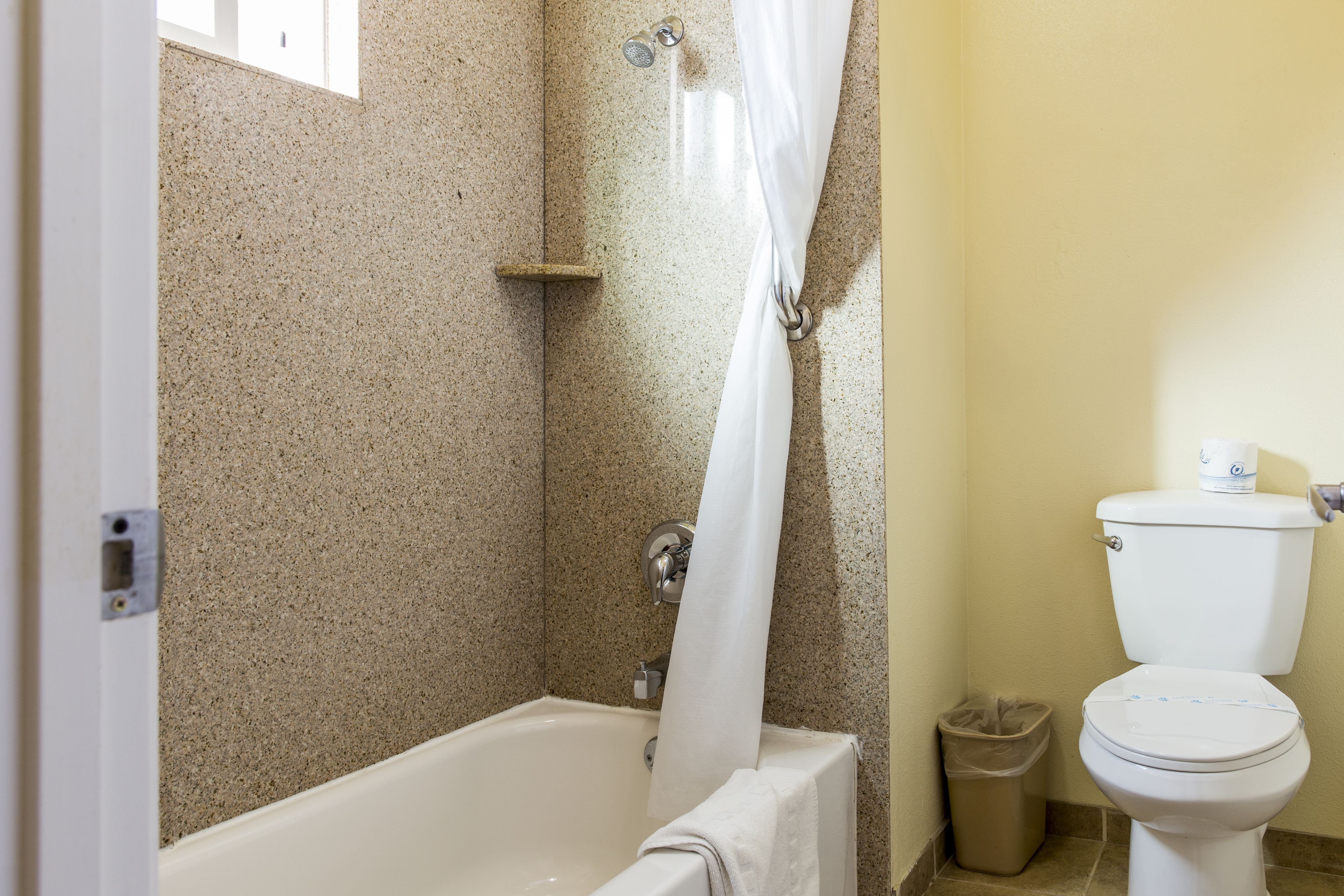 Une salle de bain équipée d’une baignoire, d’un rideau de douche, de toilettes et d’une poubelle.