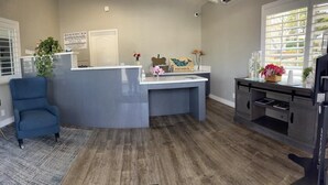 A reception area with a desk, two blue chairs, a small table with flowers, and a TV on a stand. - Ocean Palms Motel (Pismo Beach)