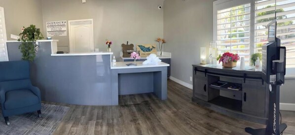 A reception area with a counter, a blue chair, and a TV. - Ocean Palms Motel (Pismo Beach)
