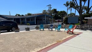 A building with a blue roof and a parking lot with several chairs. - Ocean Palms Motel (Pismo Beach)