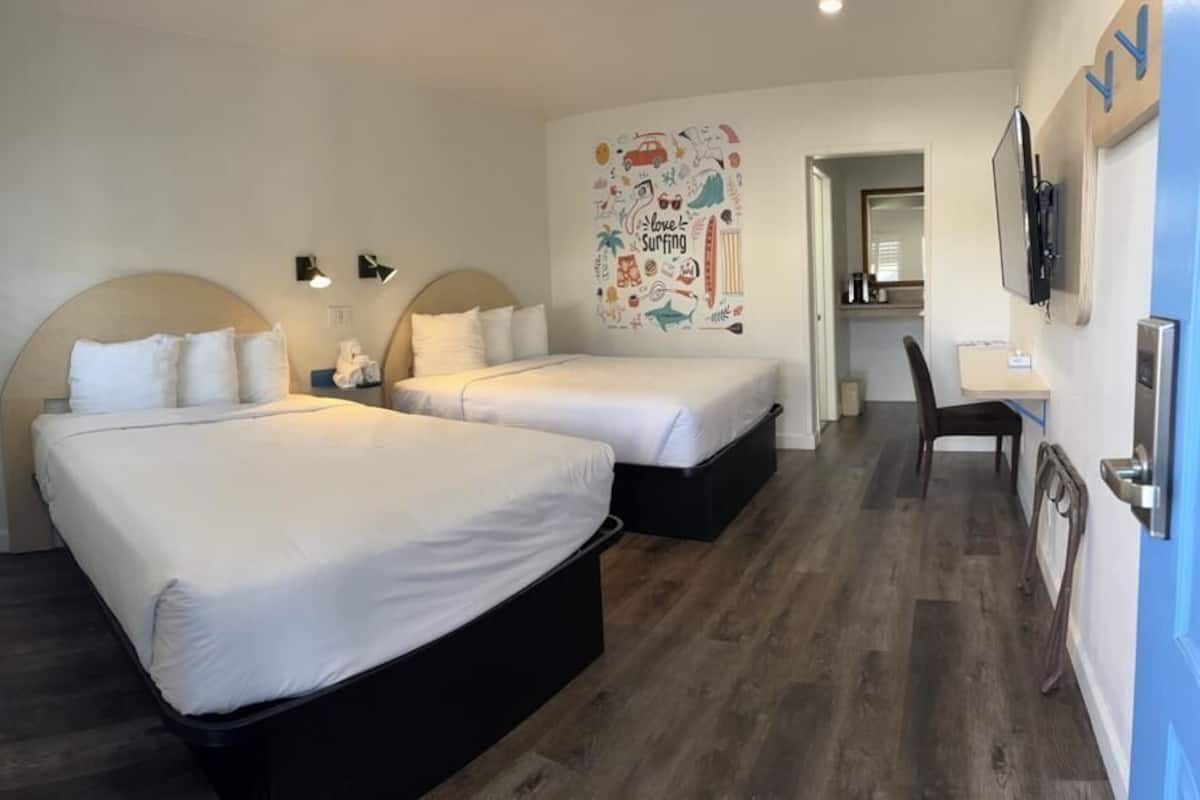 A hotel room with two beds, a desk, and a chair.