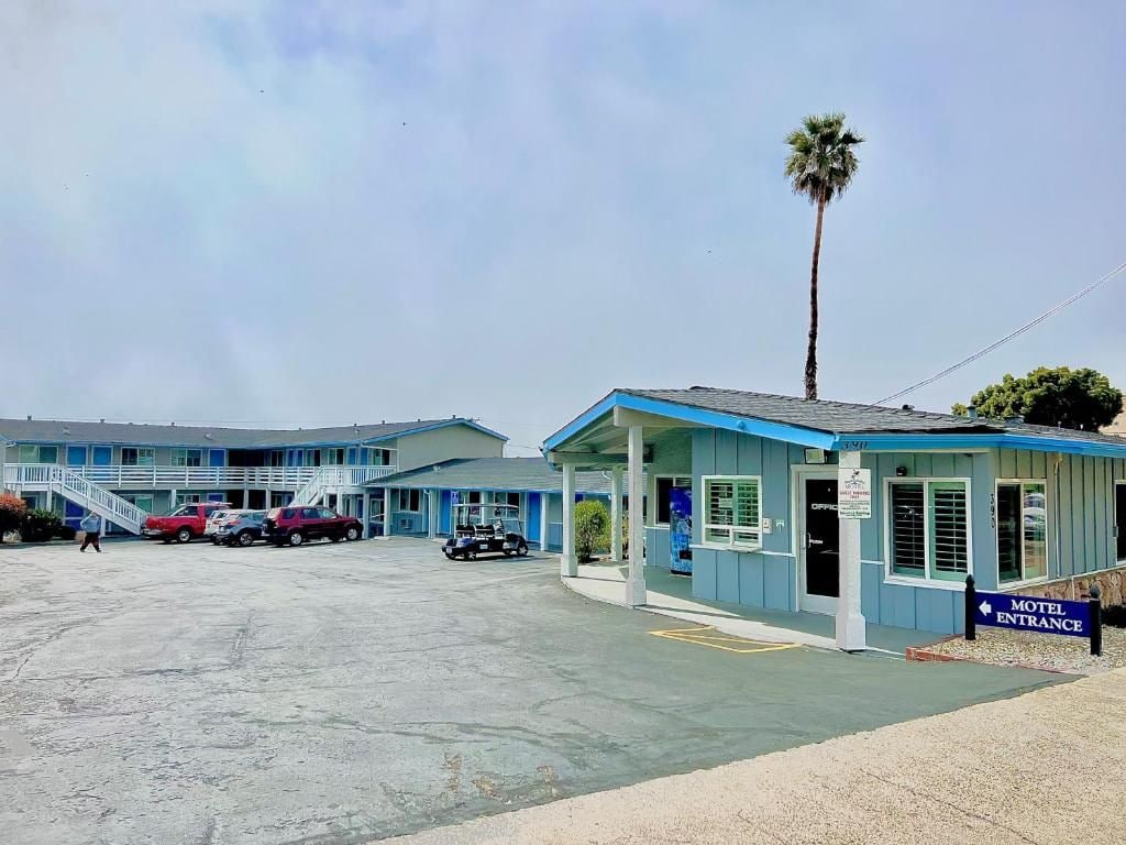 Un motel con fachada azul, un acceso cubierto y un estacionamiento con varios coches.