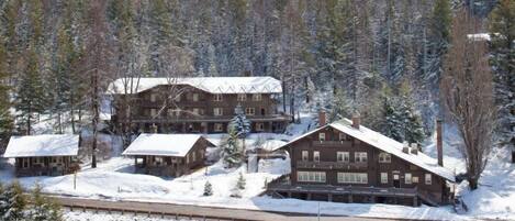 Un amplio albergue de madera con varias habitaciones, rodeado de árboles cubiertos de nieve.