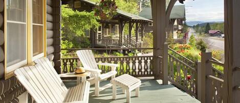 A wooden deck with Adirondack chairs and a small table, overlooking a garden and a house.