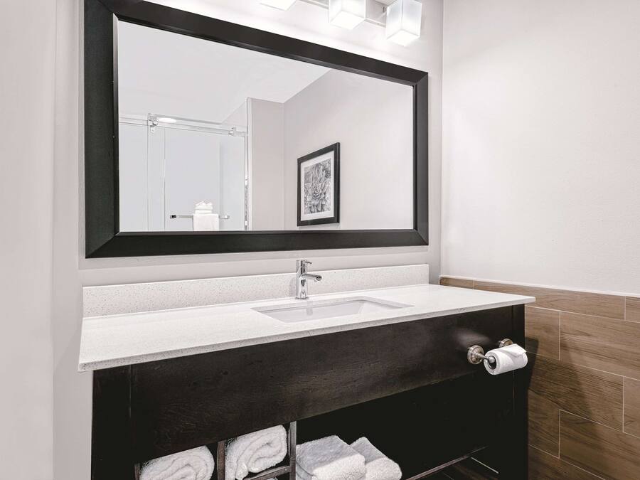 A modern bathroom with a large mirror, a white sink, dark wood vanity, and a towel rack with neatly folded towels.