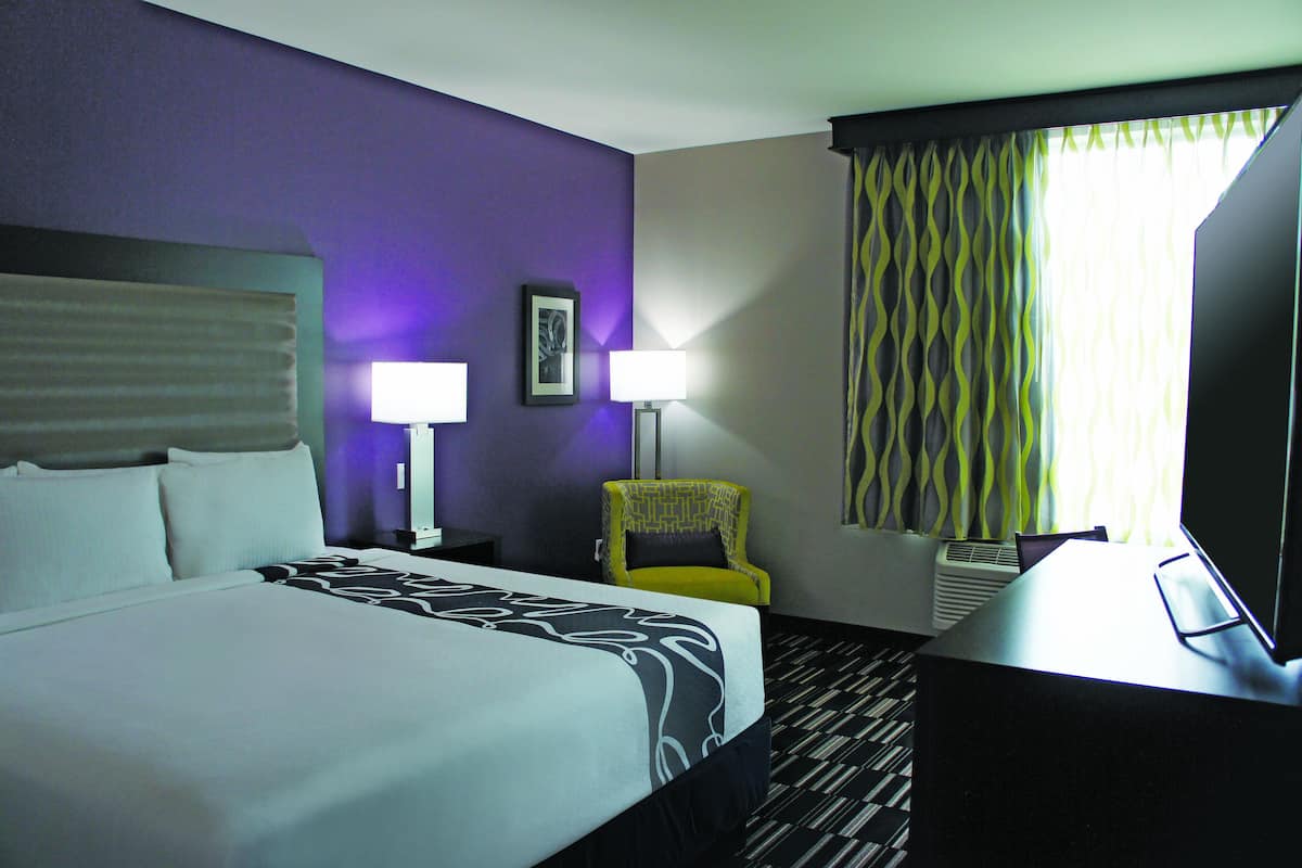 Ein Hotelzimmer mit einem Bett, zwei Nachttischlampen, einem Sessel, einem Schreibtisch und einem Fernseher.