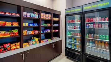 A snack and beverage vending area with multiple shelves stocked with various snacks and a Bright Side Market sign above two beverage dispensers.