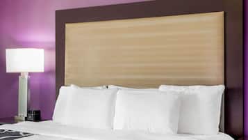 A hotel room with a large bed, white linens, a headboard, and a nightstand with a lamp.