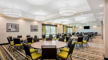 A conference room with multiple tables and chairs, large windows with curtains, and a patterned carpet.