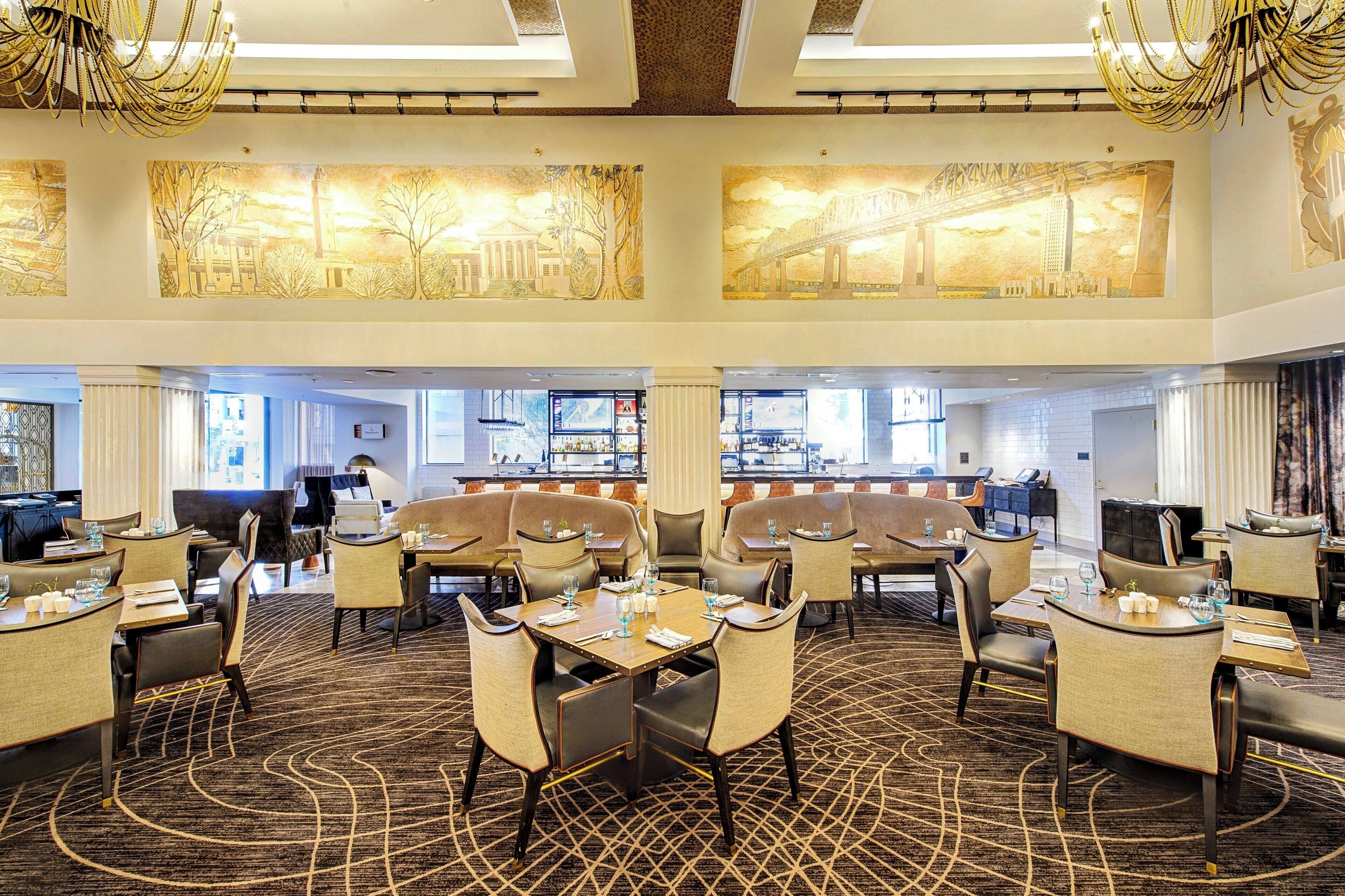 A spacious hotel lobby with multiple seating areas, a bar, and large artwork on the walls.