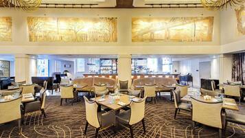 A spacious hotel lobby with multiple seating areas, a bar, and large artwork on the walls.