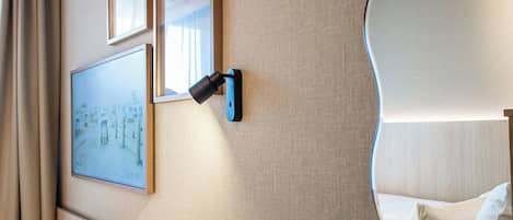 A modern hotel room with a curved wall mirror, a wooden desk, a cushioned bench, and framed artwork.