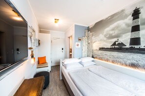 Relax in a spacious room with a large bed, seating area, and flat-screen TV, featuring a unique lighthouse painting.