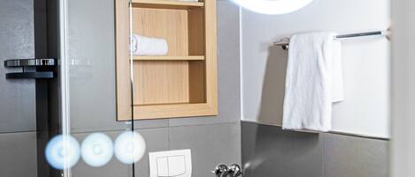 A modern bathroom with a glass shower enclosure, a wooden medicine cabinet, a towel rack, and a mirror with a circular light.