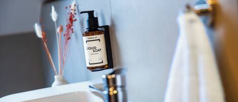A bathroom with a white sink, a mirror, and a bottle of liquid soap mounted on the wall.
