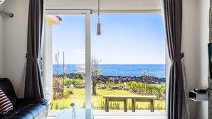 Una sala de estar con un sofá de cuero negro, una mesa de centro de vidrio y vista al océano a través de amplias ventanas.