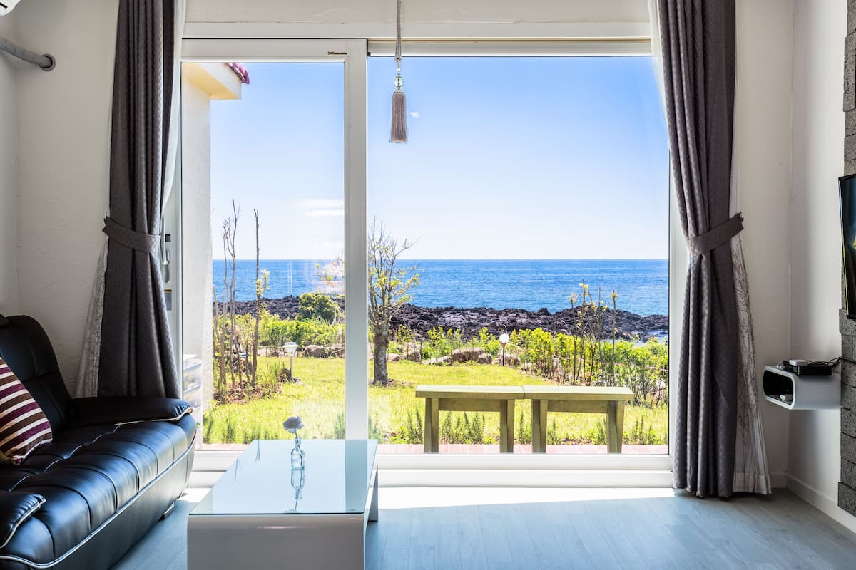 A living room with a black leather sofa, a glass coffee table, and a view of the ocean through large windows.