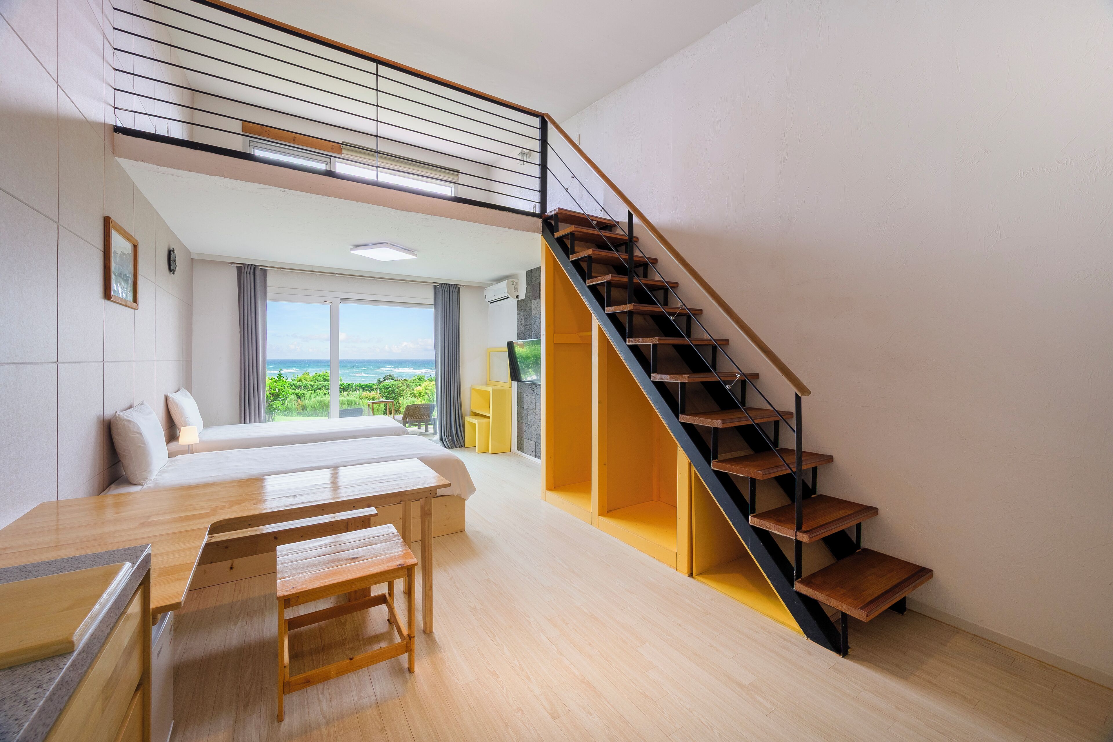 Una habitación moderna con una cama, un escritorio de madera, una escalera y vistas al exterior.