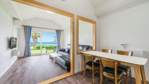 Una habitación con mesa de comedor, sillas, sofá, televisor y vistas al océano.