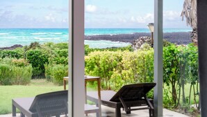 A patio with two chairs and a table, overlooking a rocky coastline and lush greenery. - Jeju Turning Point (Seogwipo)