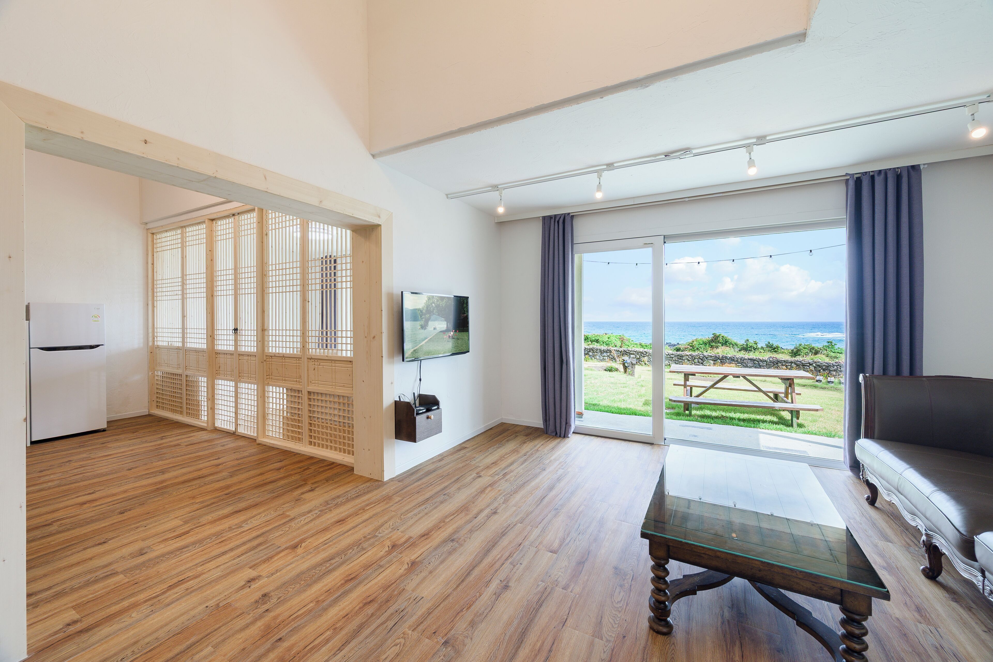 Uma sala de estar moderna com piso de madeira, uma TV de tela plana, uma mesa de centro de vidro e um sofá.